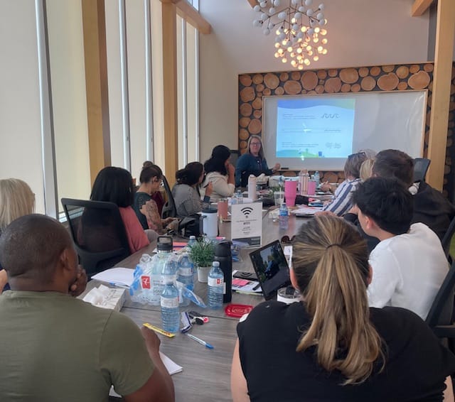 Group of people sitting at a boardroom table looking at a presentation.
