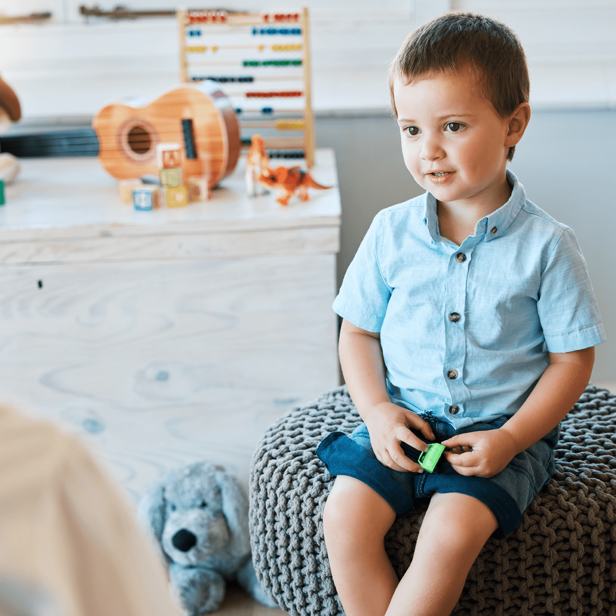 Young boy sitting on cushion across from woman in counselling-like session. Dresser with toys on top in the background.