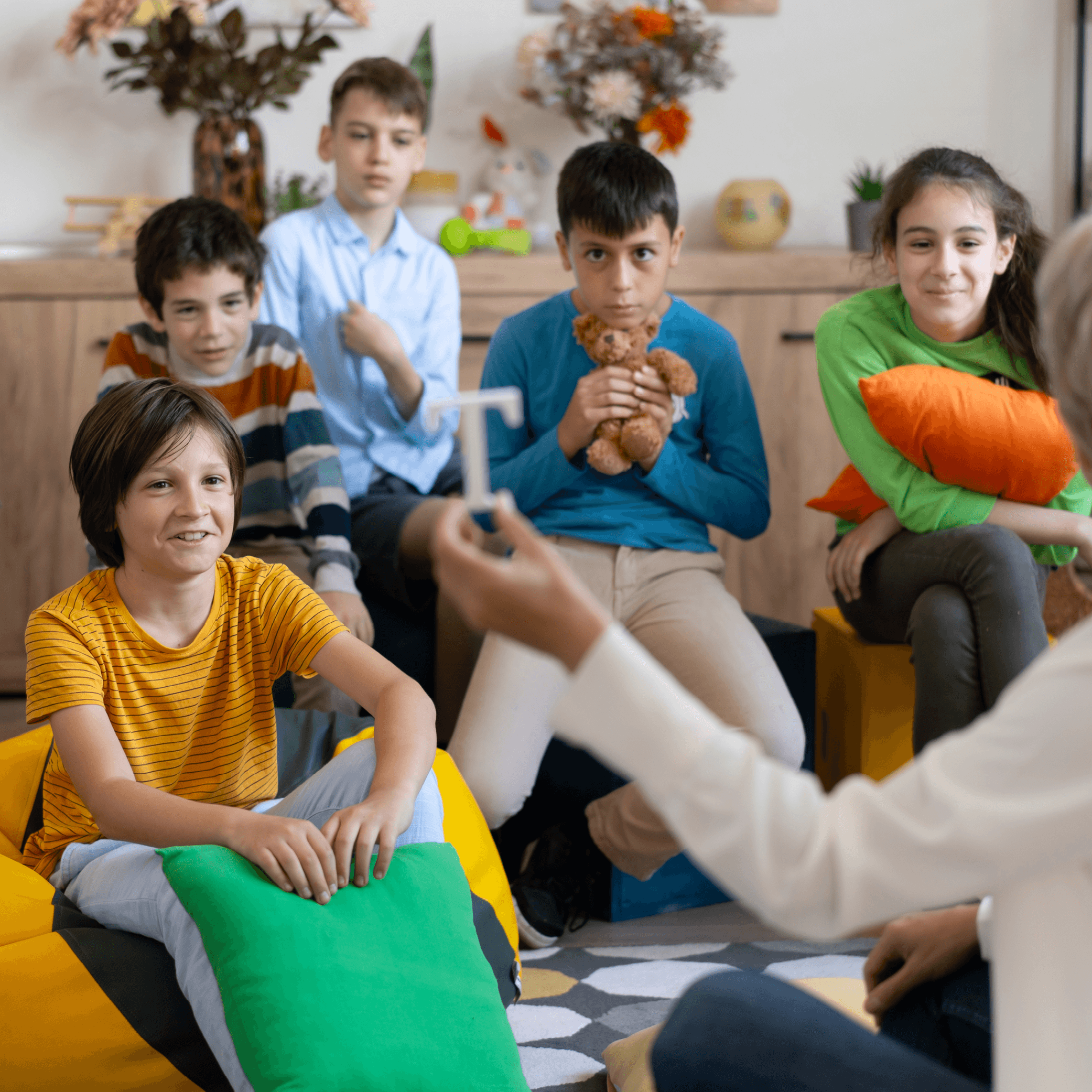 Group of children in school-like setting, smiling and sitting across from teacher.