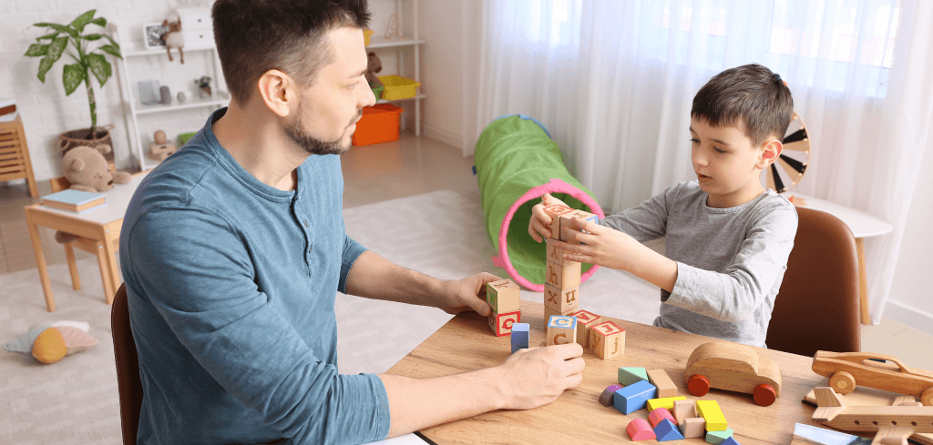 Man sitting with young boy at table playing with toys.